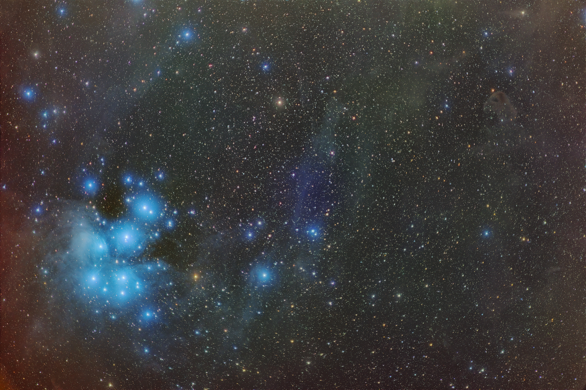 Der offene Sternhaufen Messier 45 (Plejaden) ist umgeben von bläulichen Reflexionsnebeln und schwachen Molekülwolken. Rechts oben ist der Baby-Adlernebel LDN777 erkennbar.